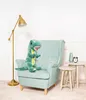 A plush dinosaur toy is sitting on a light blue armchair next to a floor lamp and two small side tables. Podgląd zdjęcia produktu