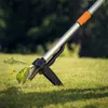 A close-up shot of a weed puller tool being used to remove a weed from a grassy lawn. Podgląd zdjęcia produktu