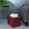A red storage ottoman sits on a tiled floor next to a gray sofa, with a plant in the background. Náhled obrázku produktu