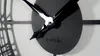 A close-up shot of a black metal wall clock with a textured center and glossy black hands. Voir les images du produit