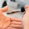 A hand holding a dropper with a drop of liquid falling onto the palm of another hand. Náhled obrázku produktu