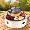 A portable charcoal grill with a teapot and food items on a wooden table outdoors. Anteprima dell’immagine prodotto