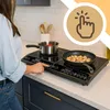 A person is using a black induction cooktop in a kitchen setting. Voir les images du produit
