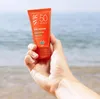 A hand holding a tube of sunscreen at the beach. Náhled obrázku produktu