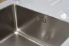 A close-up view of a stainless steel sink with a white countertop. Produktbild-Vorschau