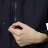 A close-up of a person's hand zipping up a dark navy jacket. Produktbild-Vorschau