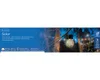 A solar-powered garden light hanging from a tree branch, with a blurred background of trees and lights. Produktbild-Vorschau
