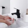 A person washing their hands in a modern bathroom sink with a black faucet. Produktbild-Vorschau