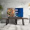 A smart TV is displayed on a wooden table in a room with a concrete wall. Produktbild-Vorschau