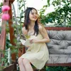 A woman is sitting on a swing bench in a garden, reading a book. Anteprima dell’immagine prodotto