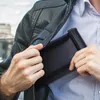 A person is putting a black Faraday bag into their jacket pocket. Podgląd zdjęcia produktu