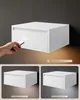 A collage of images showing a white floating nightstand, with one image featuring a hand holding a remote control pointing at it and illustrating its lighting feature. Náhled obrázku produktu