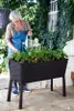 A woman is watering plants in a raised garden bed on a patio. Voir les images du produit