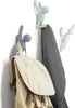 Three decorative hooks shaped like climbing figures are mounted on a white wall, holding a backpack and two pieces of clothing. Náhled obrázku produktu