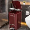 A red pedal trash can with the lid open, placed in a bathroom next to a toilet and a roll of toilet paper. Produktbild-Vorschau