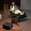 A woman is relaxing in a chair with a laptop, while a projector sits on a coffee table. Anteprima dell’immagine prodotto