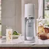 A SodaStream Terra soda maker is shown on a kitchen counter next to a glass of sparkling water and limes. Produktbild-Vorschau