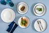 A table setting with plates, bowls, food, and glasses. Voir les images du produit