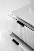 A close-up, high-angle view of a white bathroom vanity with two drawers partially open, showcasing the ribbed texture of the drawer fronts and black handles. The top surface of the vanity, which appears to be a sink basin, is also visible. Produktbild-Vorschau