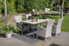 A patio dining set is arranged on a paved area next to a lawn and garden. Produktbild-Vorschau