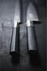 Two knives are shown in a close-up shot, with their handles in the foreground and blades extending into the background. Anteprima dell’immagine prodotto