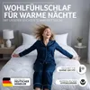 A woman in pajamas is happily sitting on a bed with a light blanket. Produktbild-Vorschau