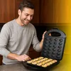 A man is in a kitchen, smiling and holding open a waffle maker with freshly baked waffle bites inside. Voir les images du produit