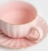 A close-up shot of a pink teacup and saucer with gold trim. Produktbild-Vorschau