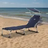 A navy blue folding lounge chair with a sunshade is set up on a sandy beach next to the ocean. Náhled obrázku produktu