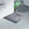 A modern bathroom setting with a grey shower tray on a tiled floor, a shower head on a textured wall, and a potted plant. Voir les images du produit