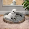 A white dog sits in a round pet bed on a pink rug, with a reflection of the dog in a mirror behind it. Produktbild-Vorschau