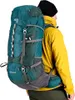 A person wearing a yellow jacket and black beanie is shown from the side, wearing a large green and teal rucksack. Produktbild-Vorschau