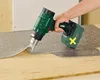A hand holding a cordless hot air gun is shown heating and lifting a piece of flooring material. Produktbild-Vorschau