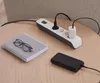 A power strip with a plugged-in adapter and a power bank sits on a wooden table next to a notebook and glasses. Náhled obrázku produktu