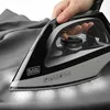 A hand is holding a Black+Decker iron as it is used to iron a gray fabric. Produktbild-Vorschau