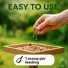 A hand is shown pouring birdseed into a bird feeder. The background is a blurred garden. Anteprima dell’immagine prodotto
