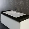 A close-up shot of a white ceramic sink with a chrome faucet mounted on a black countertop, set against a textured gray wall. Produktbild-Vorschau