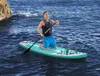A man is kneeling on a paddleboard in the ocean, holding a paddle. Produktbild-Vorschau
