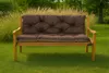 A brown cushion set on a wooden garden bench in a grassy yard with tall ornamental grasses in the background. Produktbild-Vorschau