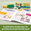 An open book with instructions for a science experiment, surrounded by various components of the experiment kit. Produktbild-Vorschau