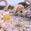 A gold metal rectangular flower stand with a bouquet of pink and peach roses on top, set against a backdrop of pink flower petals and a floral arch. Náhled obrázku produktu