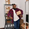 A man is holding a box next to a shelf of boxes and a step stool. Náhled obrázku produktu