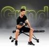 A man is sitting on a weight bench and lifting a dumbbell. The word "Grind" is written in large neon yellow letters in the background. Produktbild-Vorschau