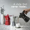 A hand pours coffee from a black Bialetti Moka pot into a white cup, with red and silver Moka pots in the background. Produktbild-Vorschau