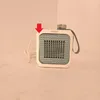 A small white and blue electric fan heater with a gray strap is placed on a light-colored surface against a plain background. A red arrow points to the top left corner of the product. Voir les images du produit