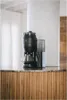A black Melitta coffee maker with a grinder attachment sits on a countertop. Náhľad obrázku produktu