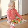 A young child is holding a wooden tray with colorful toy fruits and trees. Produktbild-Vorschau