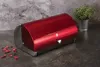 A red bread box with a silver base sits on a dark countertop next to a potted plant. Náhled obrázku produktu