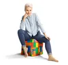 A woman is sitting on a colorful cube-shaped ottoman. Produktbild-Vorschau