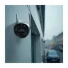 A security camera mounted on a wall during a rain shower, with a blurred street scene in the background. Podgląd zdjęcia produktu